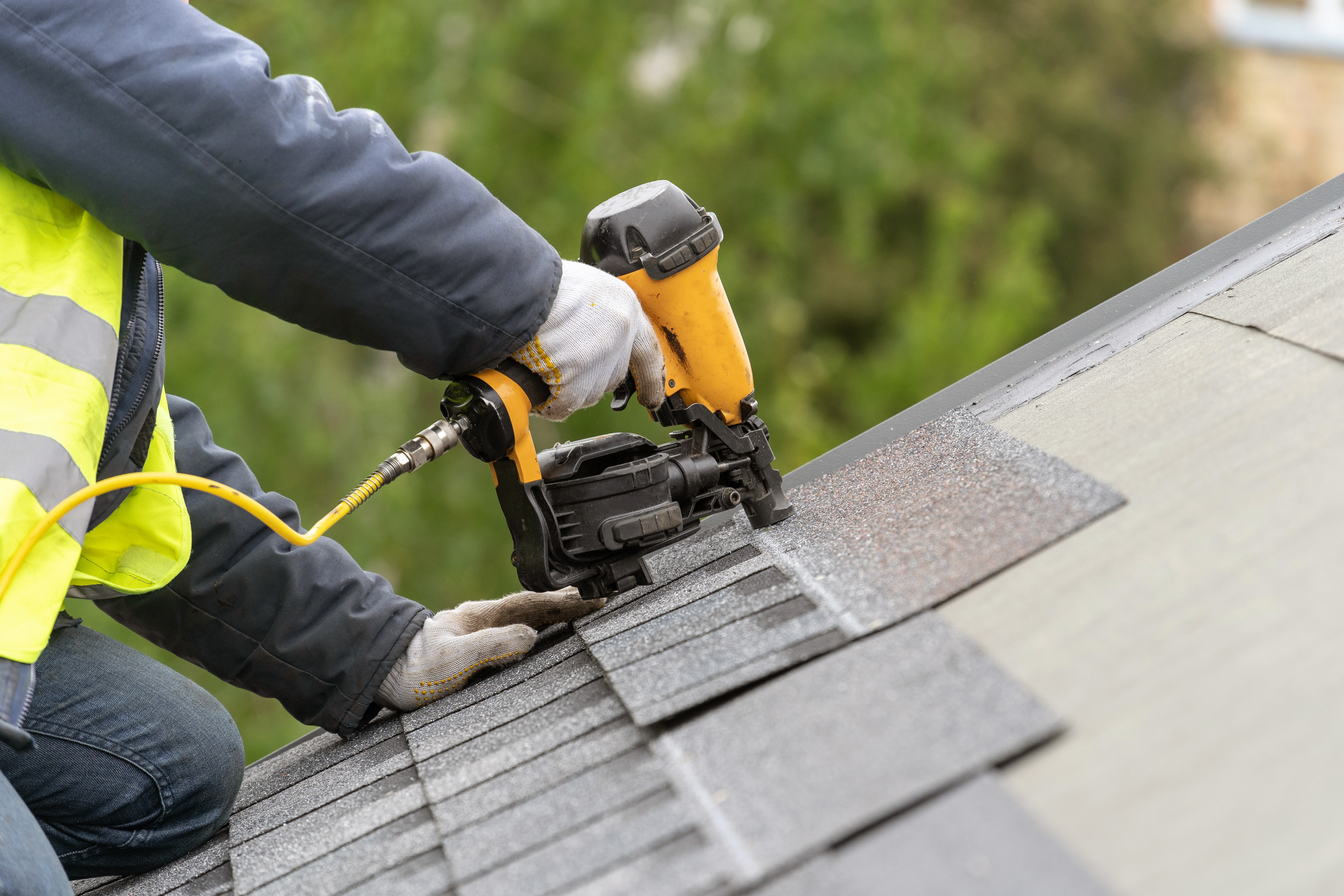 Roofer using nail gun to secure shingles